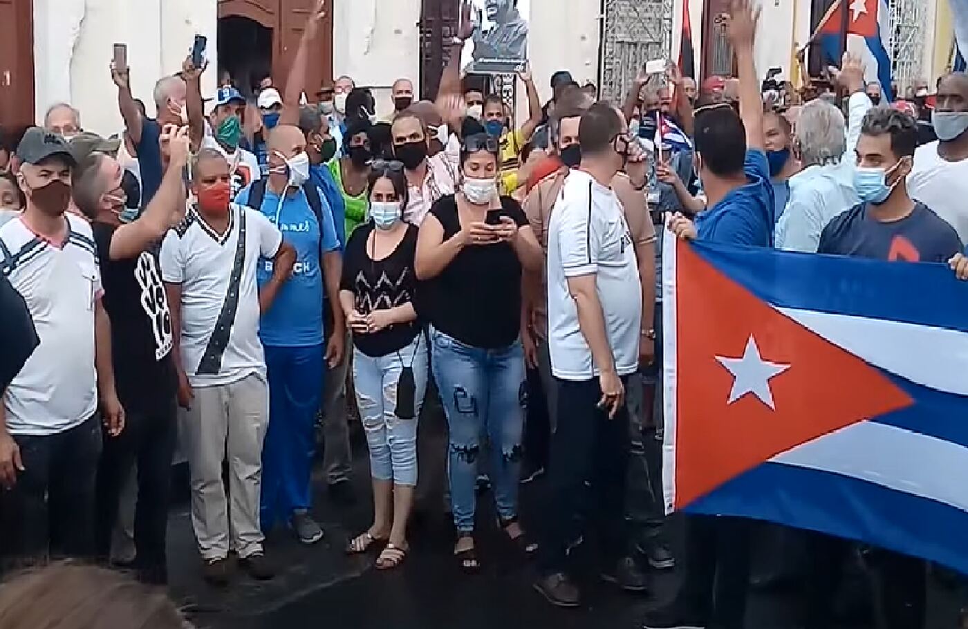 Un grupo de personas con una bandera cubana grande en una calle de Cienfuegos