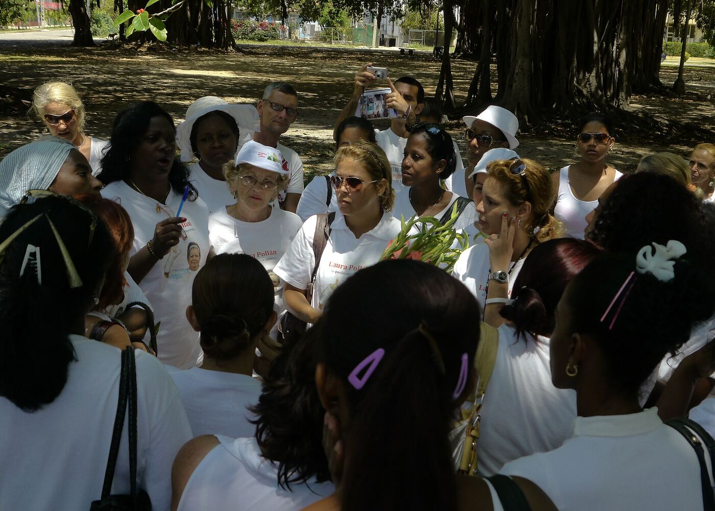 Berta Soler habla rodeada de mujeres vestidas de blanco bajo los árboles