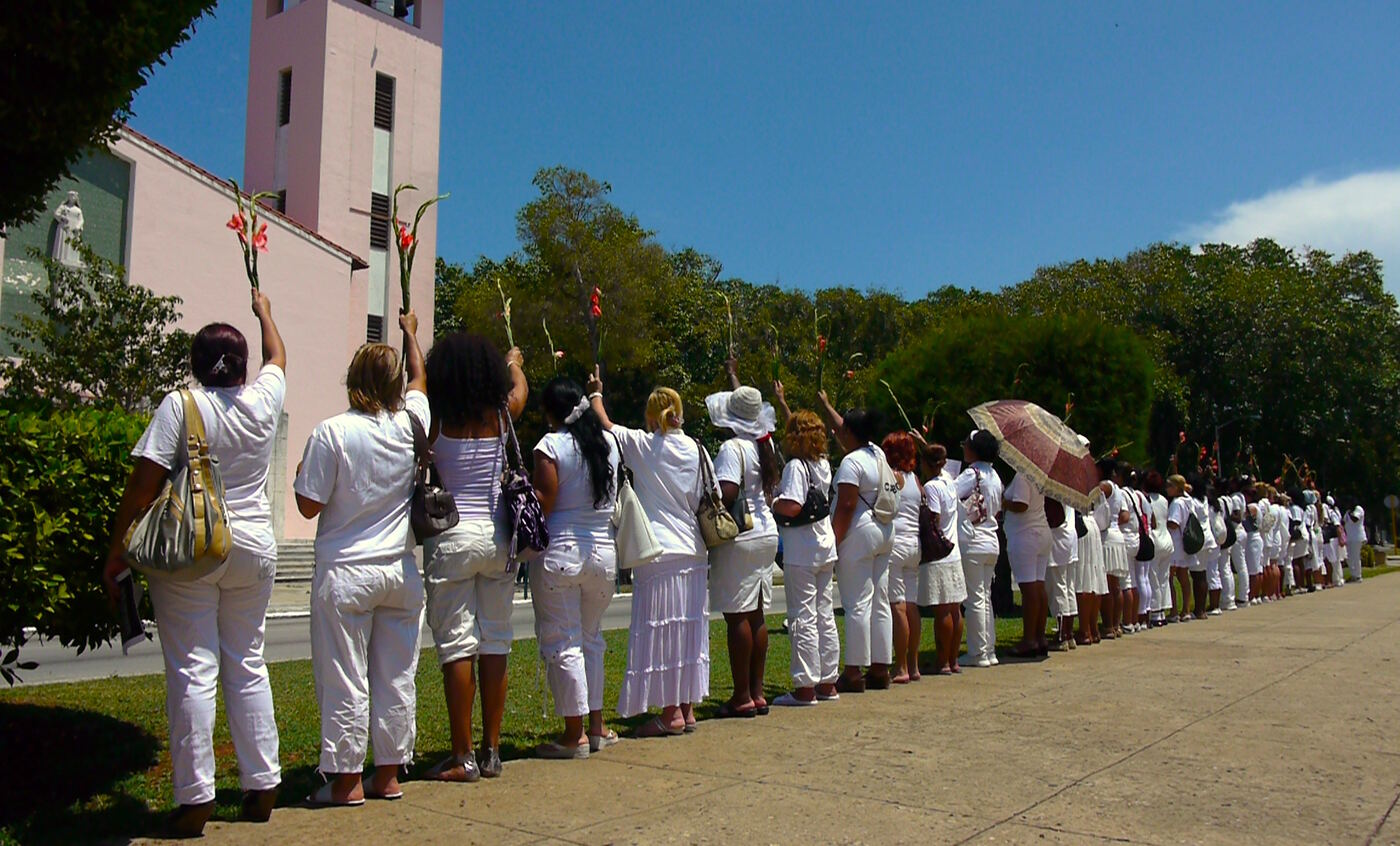 Una fila de mujeres vestidas de blanco camina por una acera de La Habana