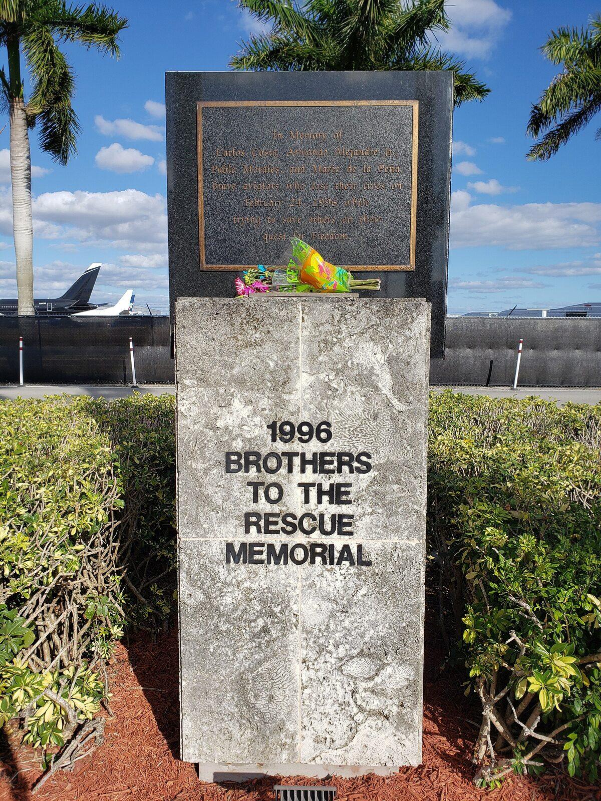 Una lápida de piedra con la inscripción 1996 Brothers to the Rescue Memorial, en el aeropuerto de Opa-locka, con palmeras y aviones al fondo